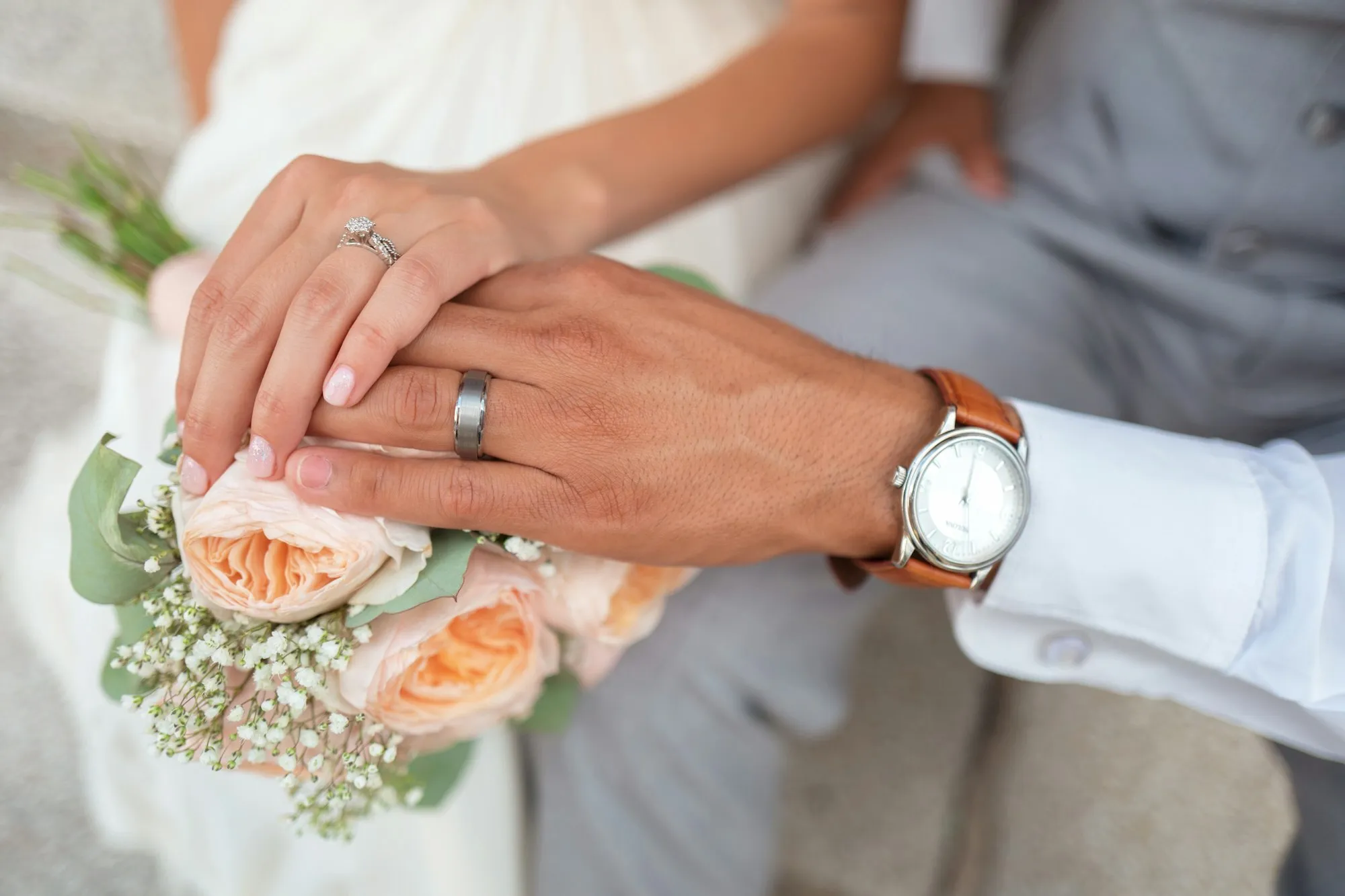 Manos de novios con anillos sobre un ramo